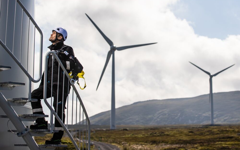 Profissional com equipamento para trabalho em altura junto a turbinas eolicas