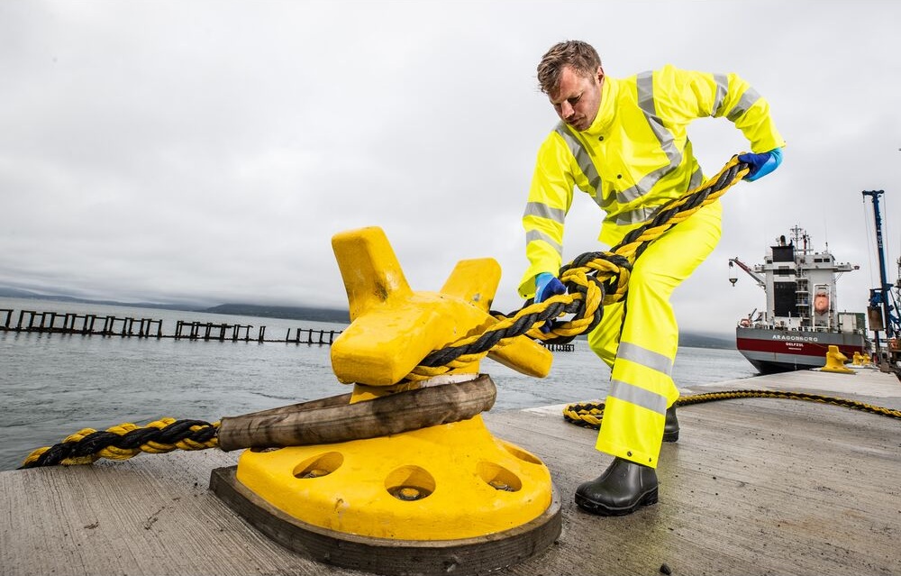 Profissional em ambiente maritimo a operar equipamento com vestuario de alta visibilidade